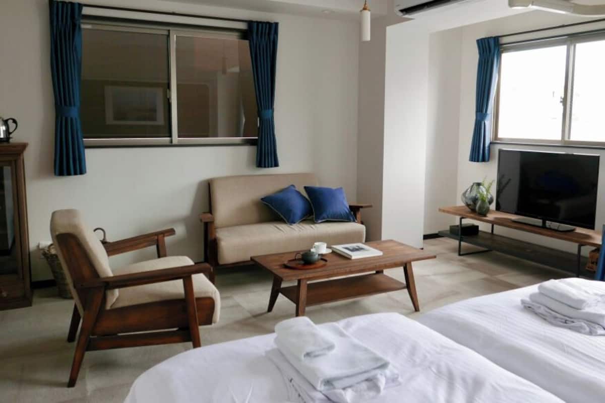 A hotel room with a bed, a sofa, a coffee table, a TV, and a window with curtains.