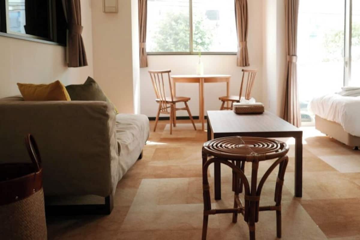 A hotel room with a sofa, a dining table with chairs, a wicker chair, and a bed.