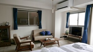 A hotel room with a bed, a sofa, a wooden chair, a coffee table, a TV, and a window with curtains. - Tokyo Sakurako Hatchobori (Tokyo)