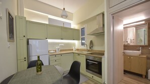 A modern kitchen with light green cabinets, a white refrigerator, a sink, and a dining area with a table and chairs. - Live As A Greek in Artemis Apartment (Athens)