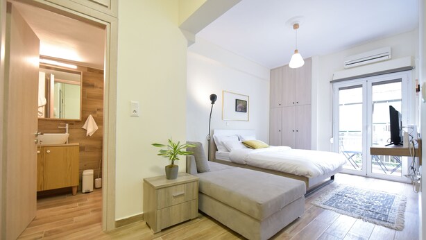 A bedroom with a bed, bedside table, and a potted plant. - Live As A Greek in Artemis Apartment (Athens)