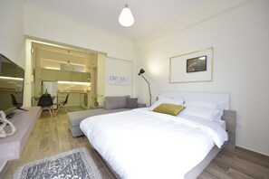 A modern bedroom with a large bed, a desk, and a chair. There is a sign on the wall that says "LIVE AS A GRIL".