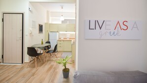A modern living room with a dining area, a kitchen in the background, and a sign on the wall that reads "LIVE AS A group". - Live As A Greek in Artemis Apartment (Athens)