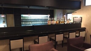 A bar area with a long counter, multiple chairs, and a television screen. - Yamanashi Grand Hotel (Chuo)