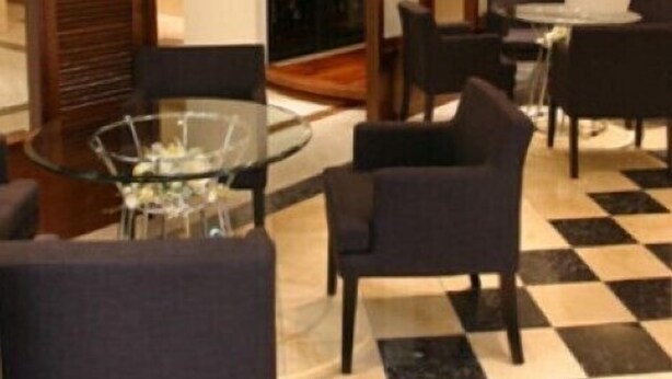 A hotel lobby with a checkered floor, a glass table, and dark chairs. - Yamanashi Grand Hotel (Chuo)