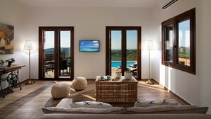 A spacious room with a large window, a wooden coffee table, a sofa, and a lamp.