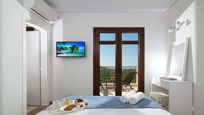 A hotel room with a bed, breakfast tray, towels, a painting, a large window, and a balcony with outdoor furniture.
