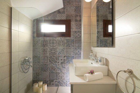 Une salle de bain avec des carreaux décorés, une douche, un lavabo avec des articles de toilette et un miroir.