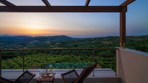 A balcony with a table and chairs, overlooking a vineyard and distant hills during sunset.