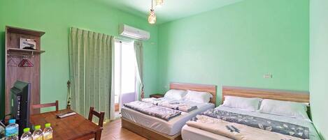A room with two beds, a wooden table with water bottles, a TV, and an air conditioning unit.
