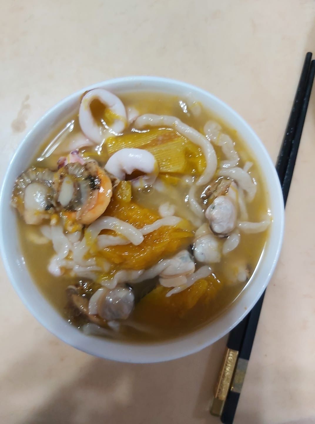 A bowl of soup with various ingredients, including mushrooms and possibly vegetables, served in a white bowl with chopsticks beside it.
