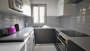 Eine kompakte Küche mit Einbauofen, Mikrowelle, Spüle und einem Fenster darüber.
