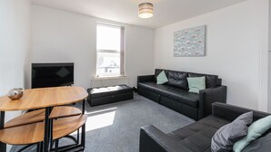A modern living room with a black leather sofa, a wooden coffee table, and a flat-screen TV. - Cherry Property - Apple Suite (Blackpool)