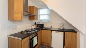 A kitchen with wooden cabinets, a gas stove, a microwave, and a dishwasher. - Cherry Property - Apple Suite (Blackpool)