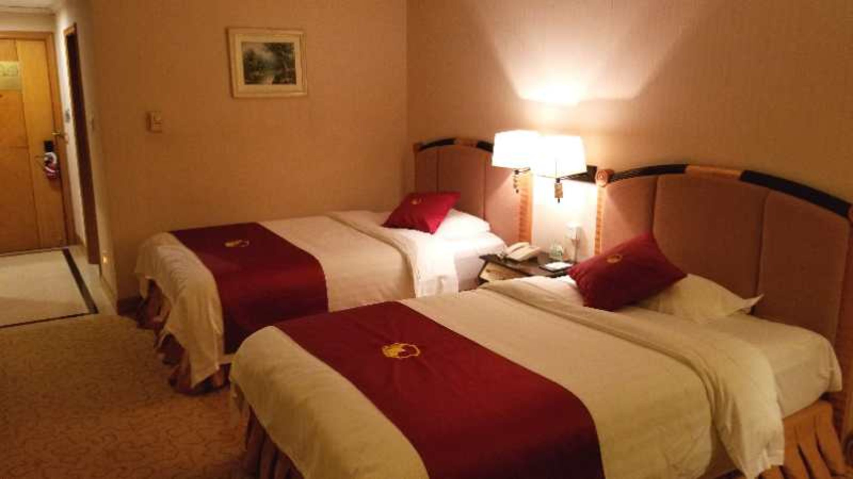 Une chambre d’hôtel avec deux lits, chacun recouvert d’une couvre-lit rouge et blanche, une table de chevet avec une lampe, et une porte située sur le côté gauche.
