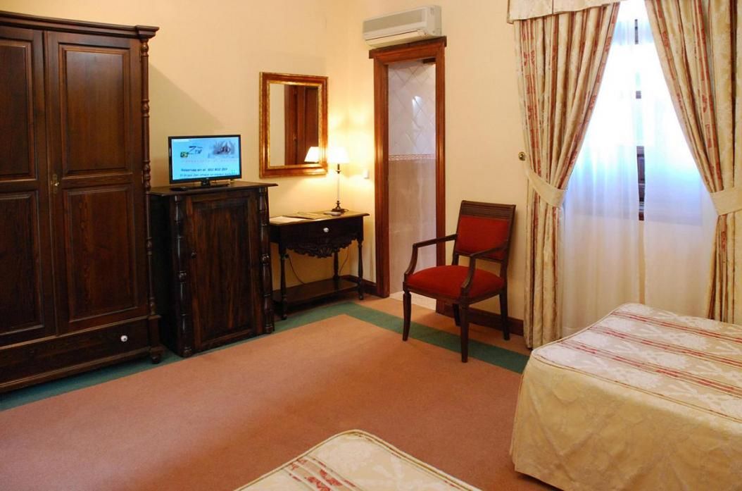 A room with a bed, a desk with a computer, a chair, a wardrobe, and a window with curtains.
