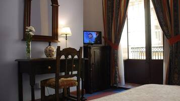 Hotelkamer met een bed, een bureau met lamp, een televisie, een spiegel en een raam met gordijnen.
