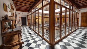 Tilava huone, jossa on ruutukuviollinen lattia, puiset kattopalkit ja suuret ikkunat, joista avautuu näkymä sisätiloihin.
