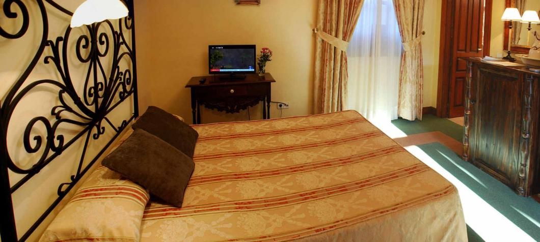 A hotel room with a bed, a television on a small table, a wooden dresser, and a window with curtains.