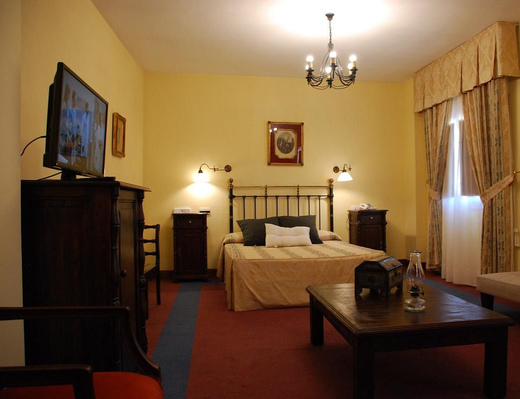 A hotel room with a bed, bedside tables, a desk, a television, and a chandelier.