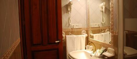 A bathroom with a wooden door, a white sink, a mirror with lights, and a towel rack.