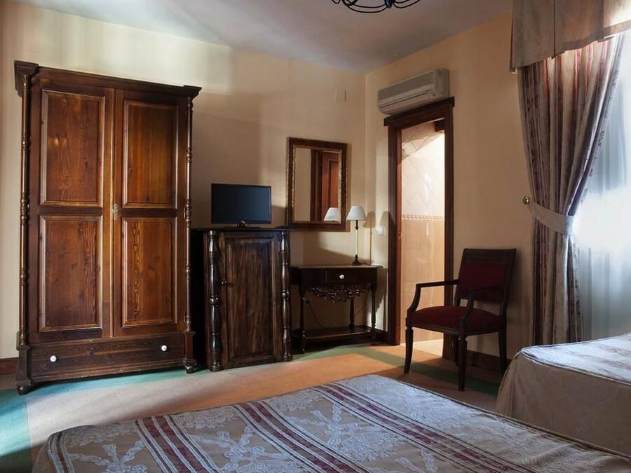 Une chambre d’hôtel avec une grande armoire en bois, un petit bureau avec une lampe, une télévision, une chaise et un lit recouvert d’une courtepointe à motifs.