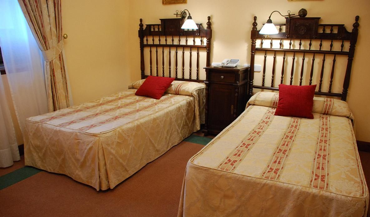 A room with two single beds, each with a red pillow and a lamp on the nightstand.
