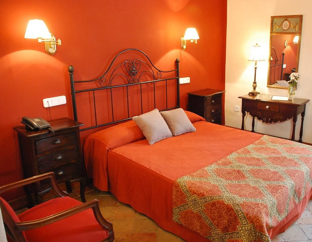 A room with a bed, two bedside lamps, a nightstand, a chair, a dresser, and a mirror on the wall.