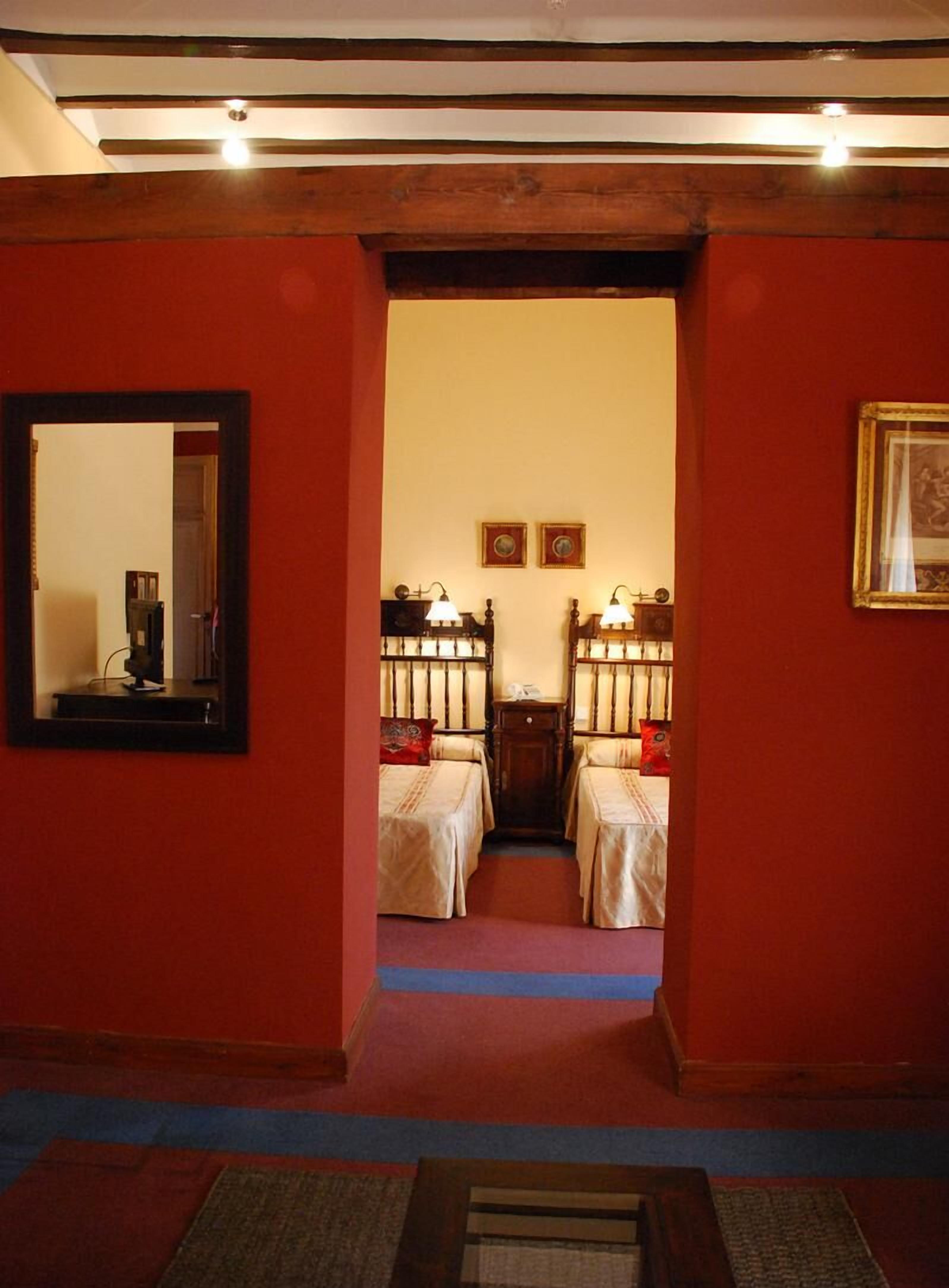 Un couloir mène à une pièce où se trouvent deux lits, un miroir et des tableaux encadrés accrochés aux murs.