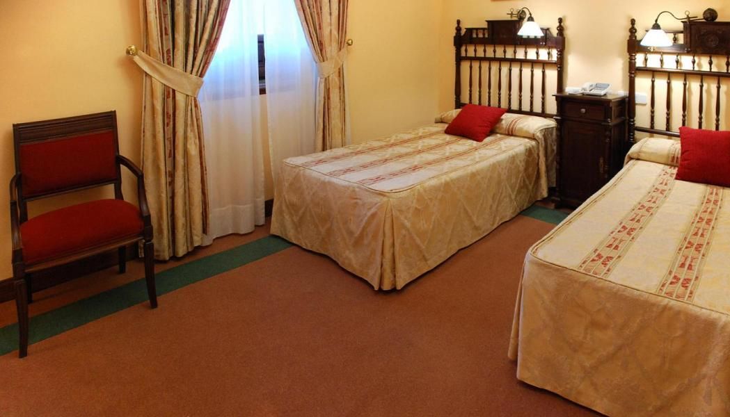 A hotel room with two single beds, a chair, a nightstand, and a window with curtains.