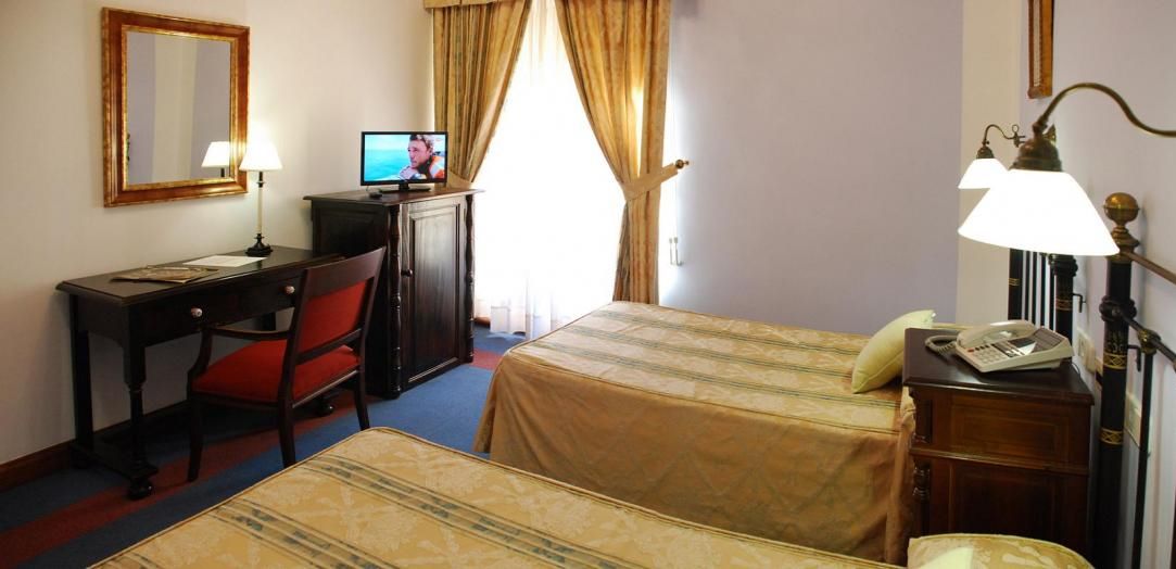 Habitación de hotel con dos camas, un escritorio con silla, televisor, lámpara y teléfono.