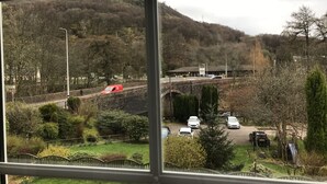 Udsigt gennem et vindue af en parkeringsplads med biler, en bro og en bygning i baggrunden.