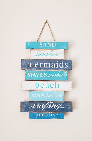 A wooden sign with words like "SAND," "mermaids," and "beach" arranged vertically. - Hawley Beachside Accommodation (Hawley Beach)