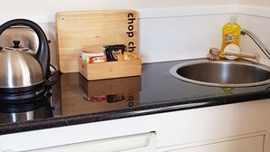 Una cocina con hervidor, tabla de cortar de madera, caja de té y botella de detergente.