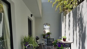 Un patio con una mesa redonda y cuatro sillas, rodeado de plantas en macetas y una pequeña mesa con un espejo.