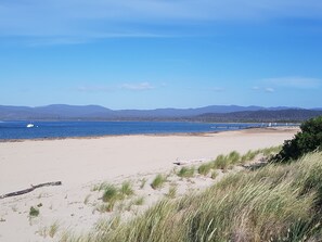 A beach with sand, grass, and a body of water. - Hawley Beachside Accommodation (Hawley Beach)