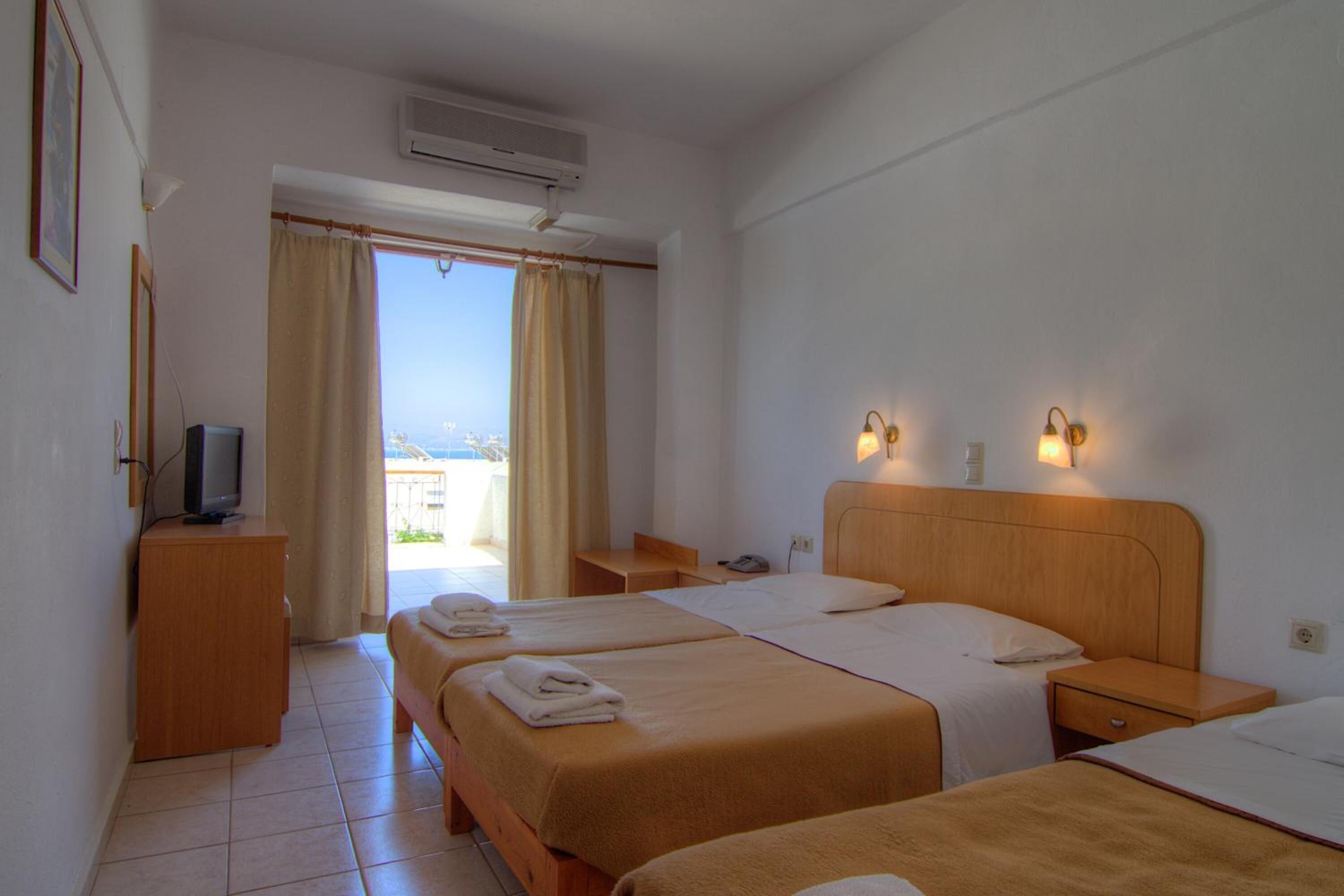 Habitación de hotel con dos camas, televisión, escritorio y vista al mar.