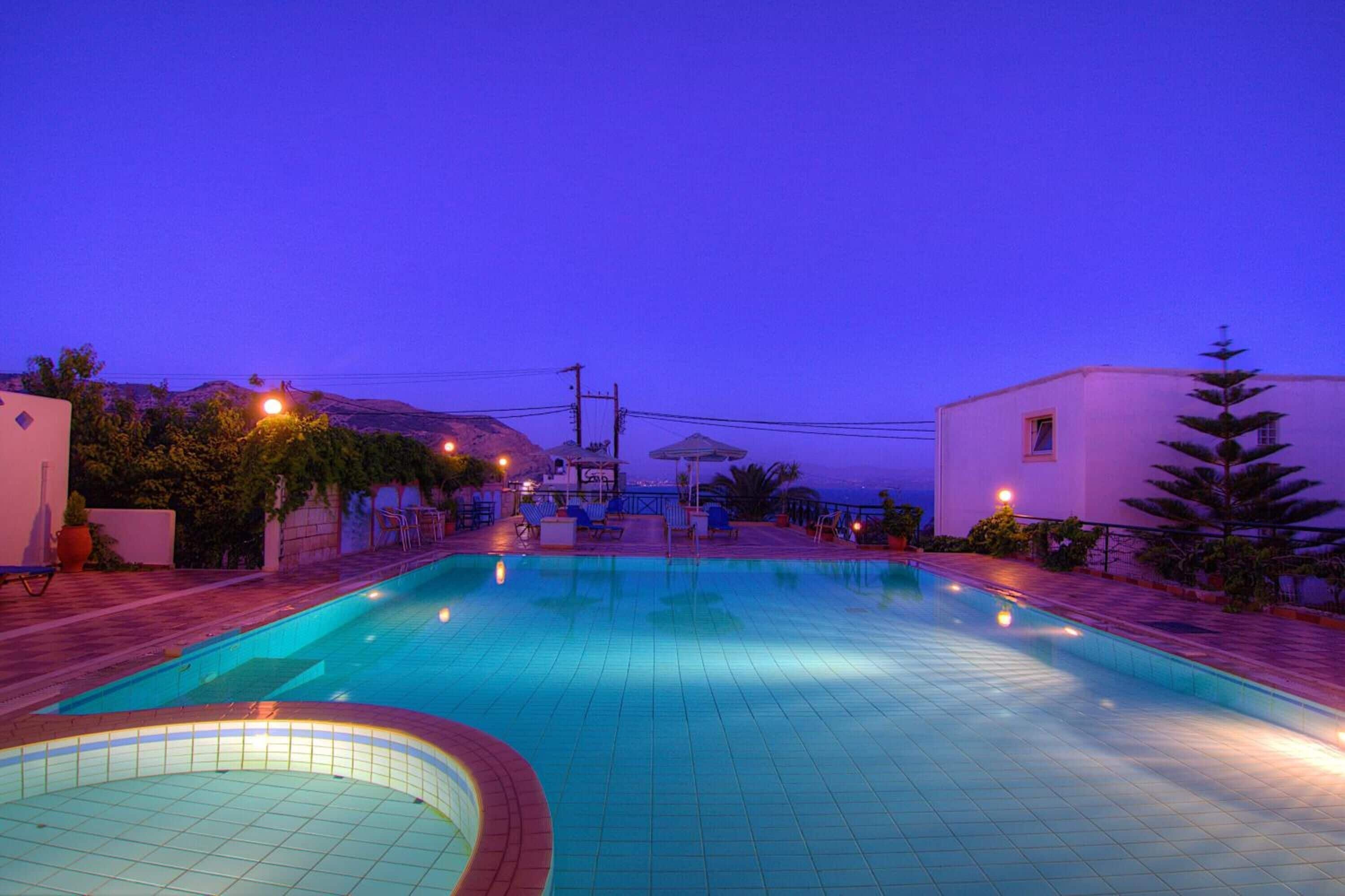 A swimming pool with a tiled deck, surrounded by a white building and a mountain in the background.