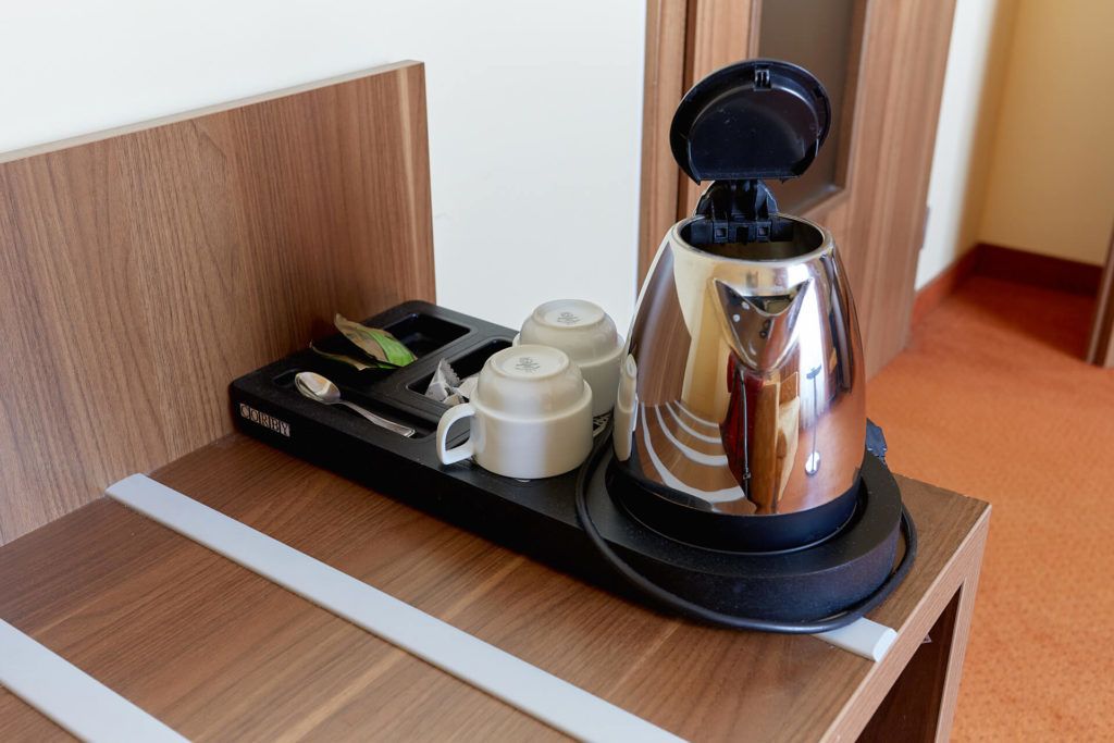 A coffee maker with a tray of cups and a spoon on a wooden table in a hotel room.
