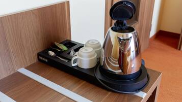 A coffee maker with a tray of cups and a spoon on a wooden table in a hotel room.