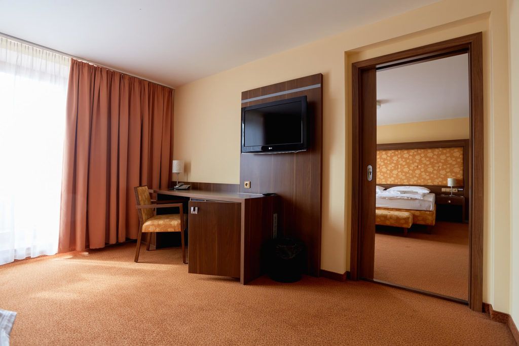 A hotel room with a desk, chair, television, and a bed.