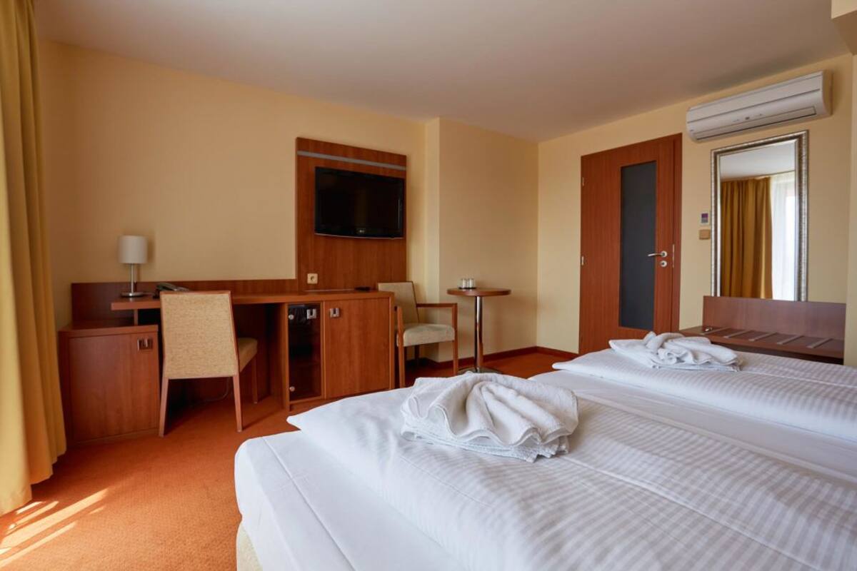 Quarto de hotel com duas camas, uma escrivaninha, uma cadeira, uma televisão e uma mesinha.