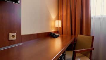 A hotel room with a wooden desk, a chair, a lamp, and a TV mounted on the wall.