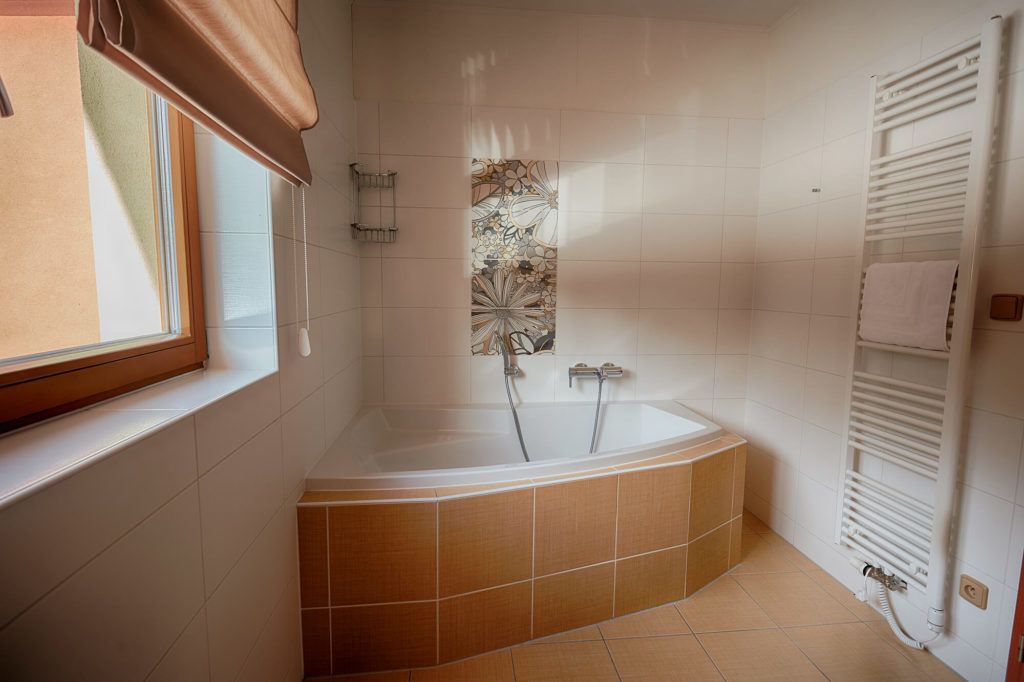 A modern bathroom with a freestanding bathtub, a window with a brown blind, and a towel rack.