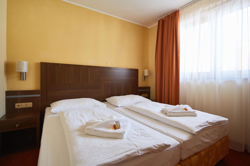 Habitación de hotel con dos camas, cabeceros de madera, ropa de cama blanca y una ventana con cortinas.