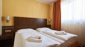 Habitación de hotel con dos camas, cabeceros de madera, ropa de cama blanca y una ventana con cortinas.