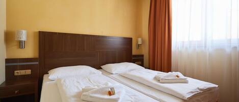Habitación de hotel con dos camas, cabeceros de madera, ropa de cama blanca y una ventana con cortinas.