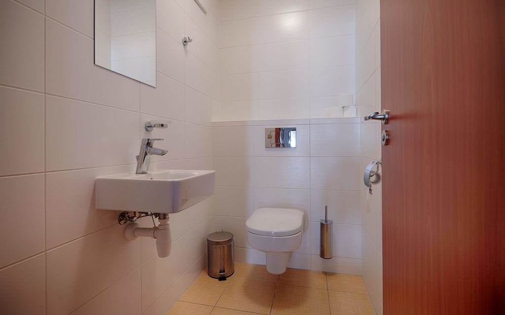 Un baño pequeño y moderno con un lavamanos, inodoro y espejo blancos.