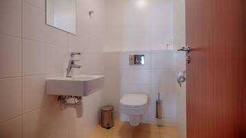 Un baño pequeño y moderno con un lavamanos, inodoro y espejo blancos.