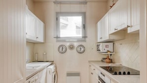 Une cuisine compacte avec des meubles blancs, un four encastré, un four à micro-ondes et un lave-linge.
